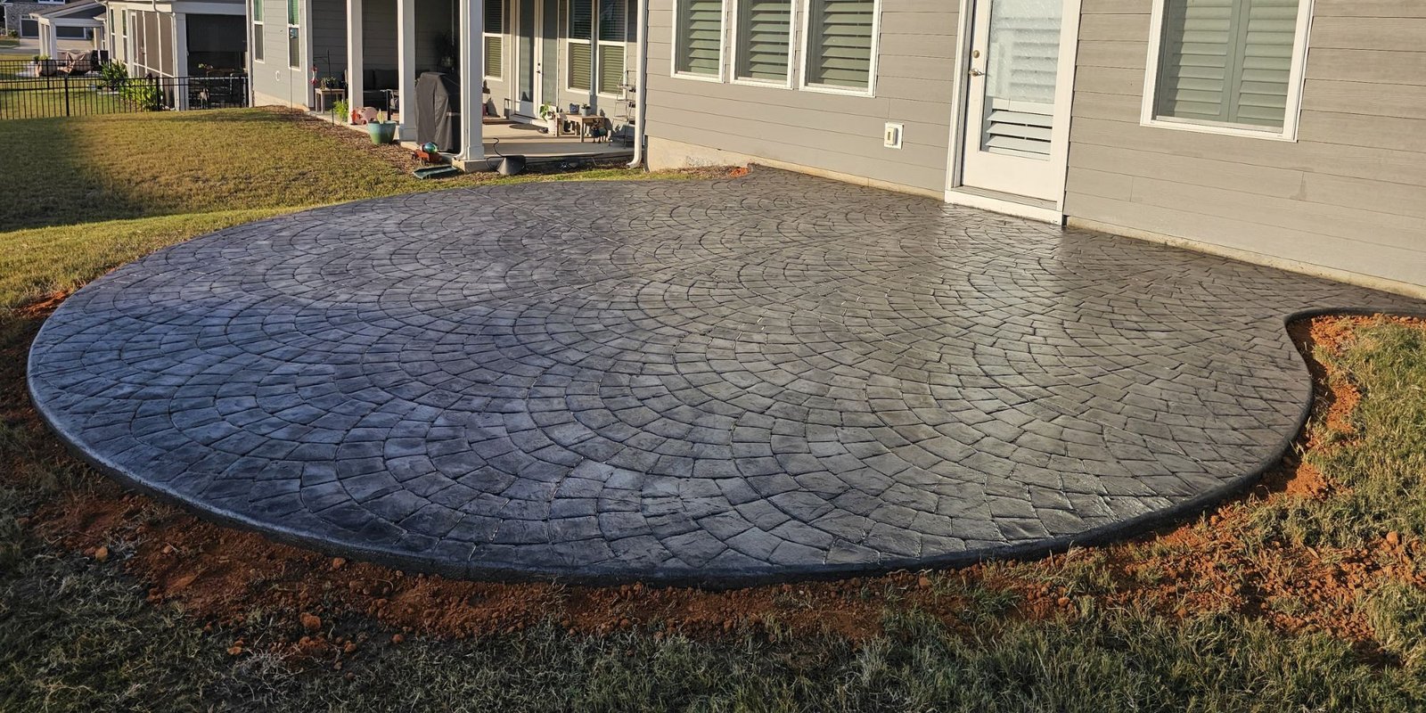 ARG stamped backyard patio with a curved edge beside a home